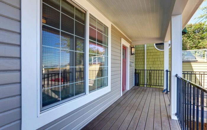 Covered front porch of a home with siding, windows, and a railing.